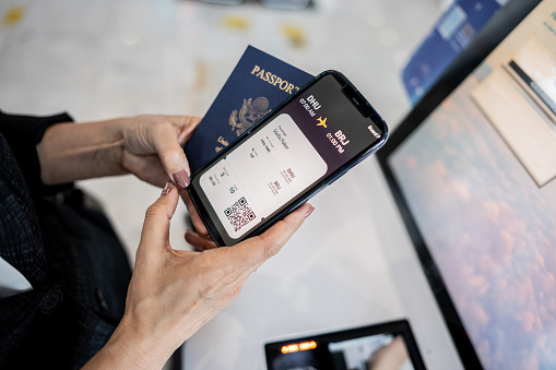 Close-up of a mature woman checking online airplane ticket on smartphone holding a passport