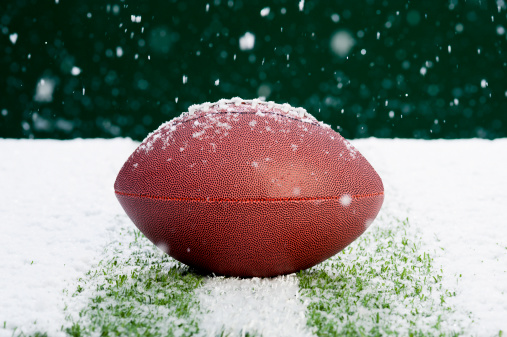 An American Football sitting on a yard line of a snow covered field as the snow falls