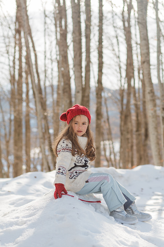 Girl sitting on a pile of snow and having some outdoor activities in the winter