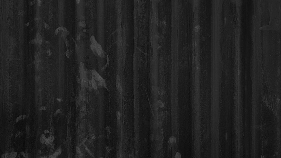 old dark black galvanized corrugated metal sheet wall with rust used as background in close up view. grey rusty  iron metal construction site wall.