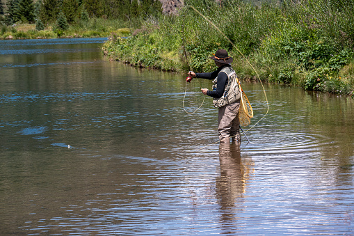 An adult woman, dressed in full fly-fishing attire, fishes Ten Mile Creek,  west of Frisco, Colorado, in the Rocky Mountains, during the month of August.