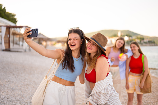 Four teenage girls in a summer clothes taking a selfie with a smart phone on an empty beach early in the morning in a summertime in Primosten, Croatia.
