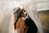 Bride and groom kissing tenderly under a long veil in nature