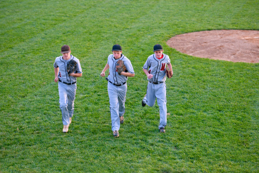 High angle view of three baseball players running off the playing field and toward the dugout in evening light.