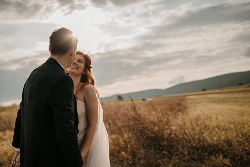 Romantic wedding couple standing and looking at each other in nature with beautiful sky in background