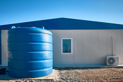 Blue plastic water tank stands next to prefabricated industrial building. Newly built single storey prefabricated industrial building. Prefabricated office container building at construction site