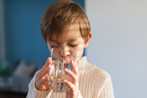 A child drinks water from a glass in the living room.