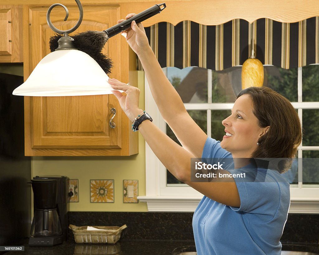 A woman using a feather duster to clean a light shade Woman Cleaning The Lamp In Kitchen With Dusting Brush Duster Stock Photo