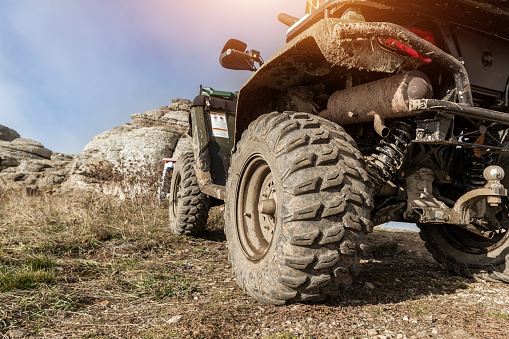 Close-up detail bottom POV view 4x4 awd ATV vehicle on dirt gravel unpaved road in autumn at misty mountain top. Offroad car mountain safari adventure nature trial journey concept. Quad bike rental.