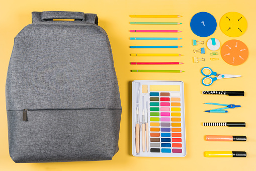Education, learning, back to school background. Knolling composition with gray backpack and different school stationery supplies on yellow background. Top view, flat lay.