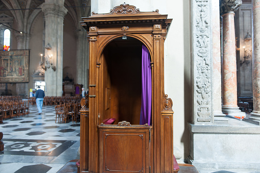 Como Italy - May 6 2011; Wooden confessional booth open with purplke curtain inside church_
