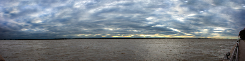 Panoramic image composed by 9 photographys. Of the Parana river, and birds. Reduced to 10400 px long side, to upload here. On a cloudy and windy day, at the morning of the 22 august, 2023, viewed from the river bank.