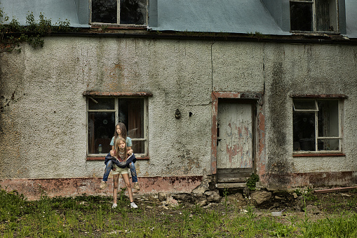 Two young, impoverished girls playing piggyback in their front yard. Posed by models.