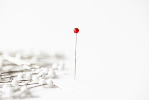 Pins on white background. Red needle is standing out of crowd.