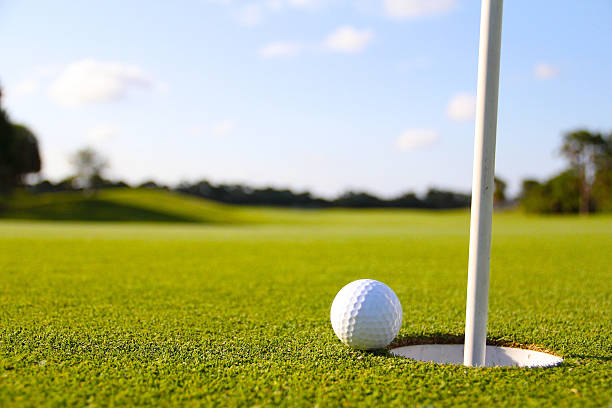 golf ball next to the hole and flag Golf ball sitting on the edge of the hole putting green stock pictures, royalty-free photos & images