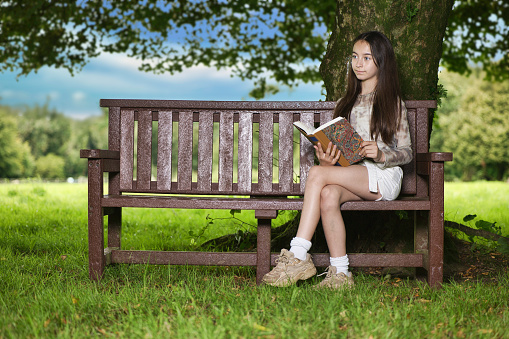 Pre-teen girl sitting outdoors to read her book.