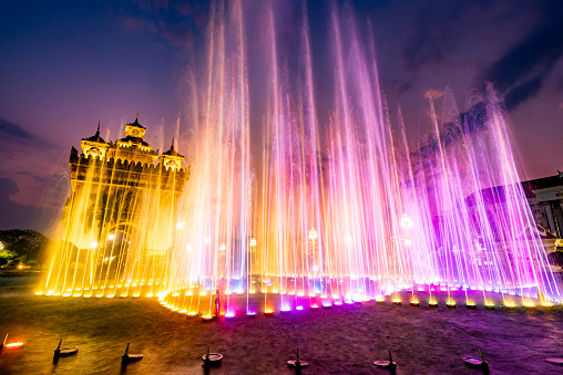 Beautiful,colorful light and fountain water display,synchronized with patriotic Lao music from nearby speakers,the Patuxay War memorial illuminated in the background.Performed every day,at dusk.