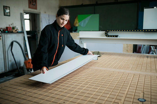 Woman worker placing a acrylic sheet on flatbed of a cnc engraving machine. Female worker working in a signage manufacturing unit.