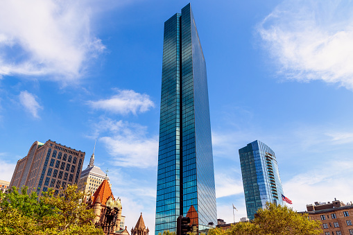 Boston, Massachusetts, USA - August 29, 2023: The 200 Clarendon Street skyscraper, formerly named the John Hancock Tower, has 62 stories and is 790 feet (240m) high. It is the highest building in Boston and all of New England. Located in Boston's Back Bay neighborhood, it was completed in 1976. It is next to Copley Square and its Trinity Church, visible in lower left group of buildings. The Raffles Residences tower, luxury condominiums and hotel, is in the background.