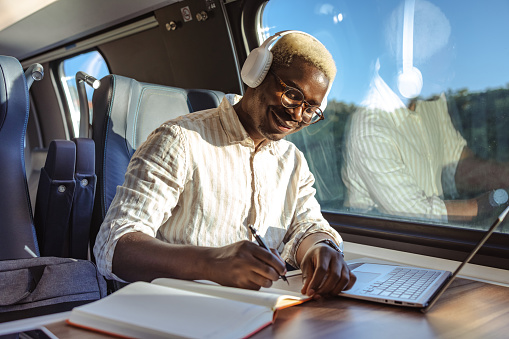 African American young modern man commuting by the train and using a laptop