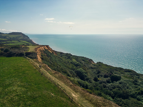 Drone aerial view of teenagers hiking in Dorset, United Kingdom. They are walking on the path on cliff by the sea .\nShot with DJI Mini 3 Pro