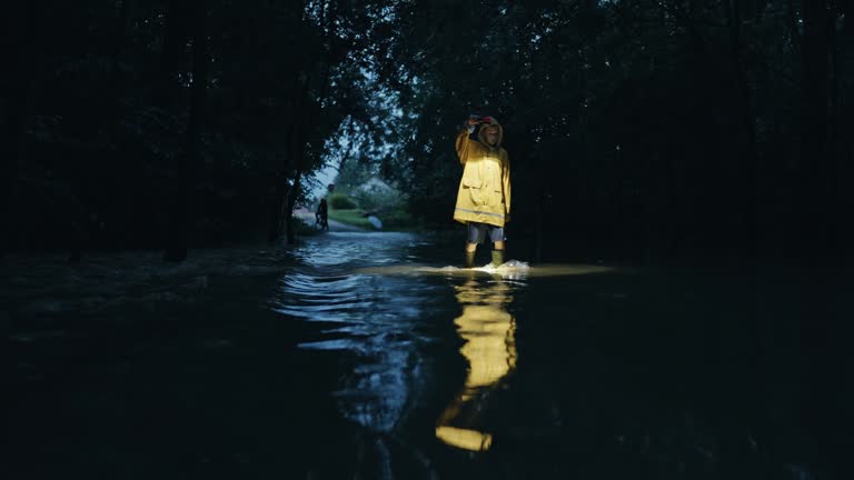 SLO MO Young Boy Walking with Flashlight in Forest's Flooded Plain with Flowing Water on Rainy Night