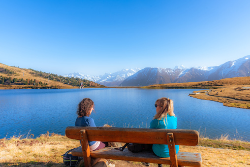 Two women sitting on a wooden bench while enjoying the nature landscape. Nature and travel concept.