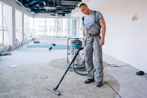Demonstrating his attention to detail, a young man carefully uses a vacuum to clean the carpet following its installation