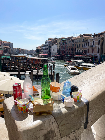 Grand Canal, Venice, Italy - July 14, 2023: Stock photo showing close-up view of litter left on bannister of the Rialto Bridge (Ponte di Rialto) whilst boats travel on the Grand Canal, Venice, Italy.