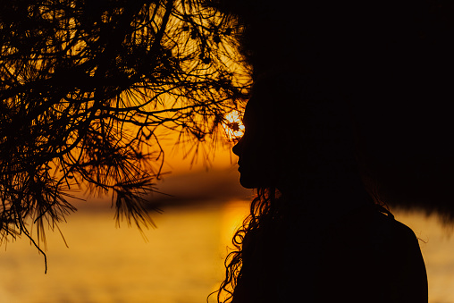 Back view backlight portrait of a single woman watching a sunset on the city with a warm light in the background