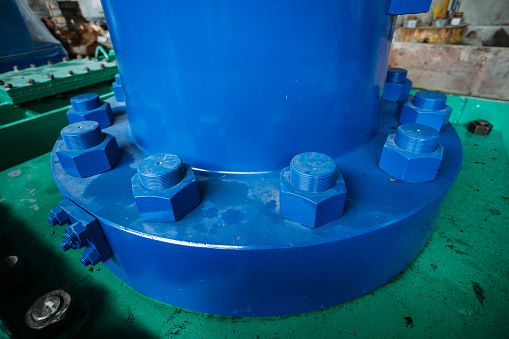 Bolts and nuts on blue flange of joint of hydraulic jack on hydroelectric power plant.