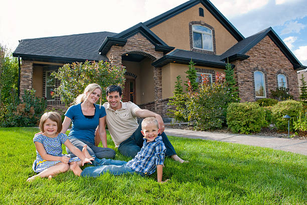 Smiling family on front lawn of a house Family of four, including mother, father, and son and daughter sits in front of their beautiful home. They are proud and smiling to be in such a great place. in front of stock pictures, royalty-free photos & images