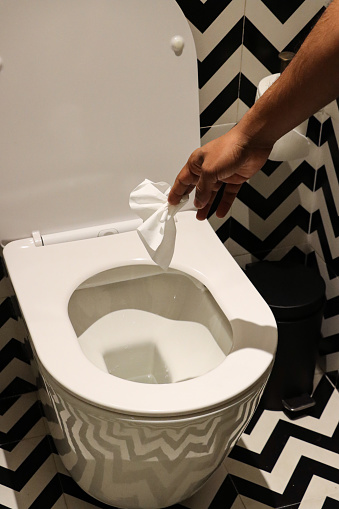 Stock photo showing luxury bathroom with black and white zig-zag patterned wall and floor tiles with flushing toilet having paper tissue being dropped into the toilet bowl.