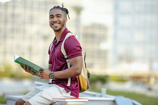 Smiling male student holding books and reading notes