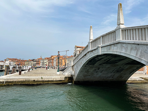 Stock photo showing close-up view of the Ponte San Biasio delle Catene, pedestrian bridge spanning canal flowing into Venice Lagoon waterfront, Venice, Italy.