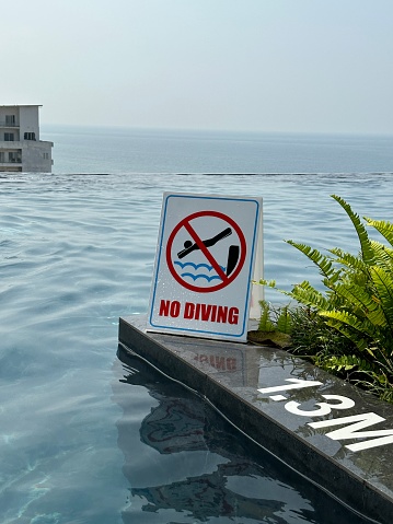 Stock photo showing close-up view of infinity swimming pool with no diving warning sign for health and safety to prevent accidents and potential drowning hazard for swimmers