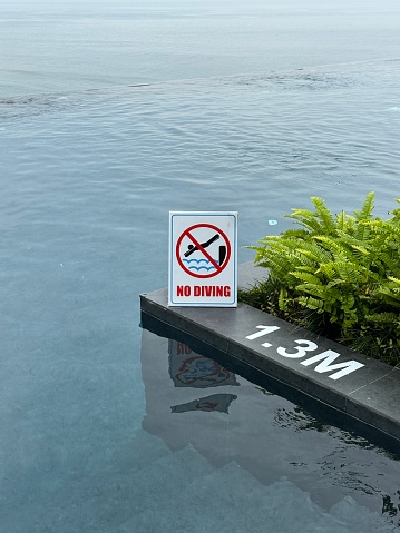 Stock photo showing close-up view of infinity swimming pool with no diving warning sign for health and safety to prevent accidents and potential drowning hazard for swimmers