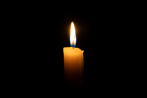 an orange candle burns in the dark on a black background. The concept of memory and sorrow.
