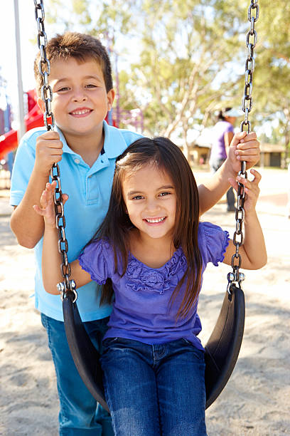 menino e uma menina brincando de balanço no parque - swinging sister family child - fotografias e filmes do acervo