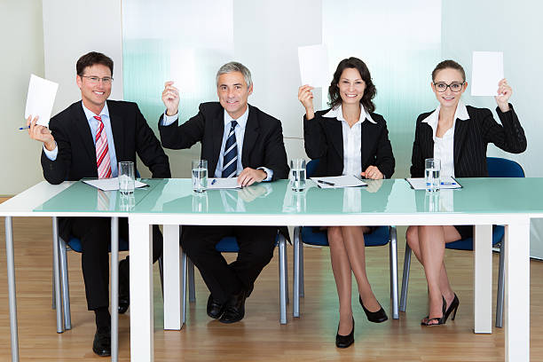 Group of judges holding up blank cards Group of four stylish professional judges seated at a long table holding up blank cards for their scores women satisfaction decisions cheerful stock pictures, royalty-free photos & images
