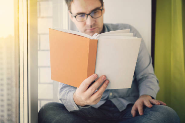 istock Young man sitting next to a window reading a book and enjoying his leisure time 1651636762