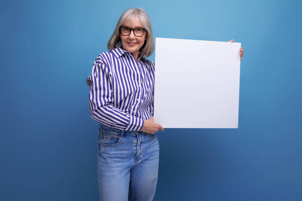 istock Successful grey-haired mature old lady shows blank billboard with mocap on bright studio background 1651643770