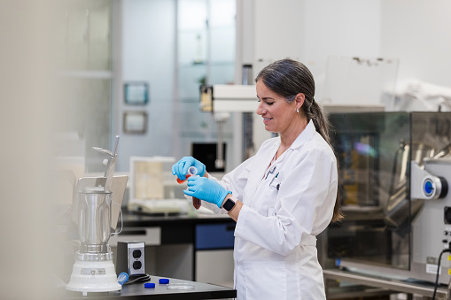 The mature female scientist holds test tubes carefully and smiles while she works on her experiment.