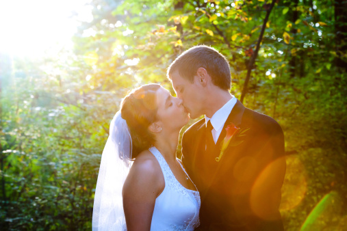 A nostalgaic, instant classic aesthetic: bride and groom pose for a portrait with strong sun flare brightening and coloring the frame.