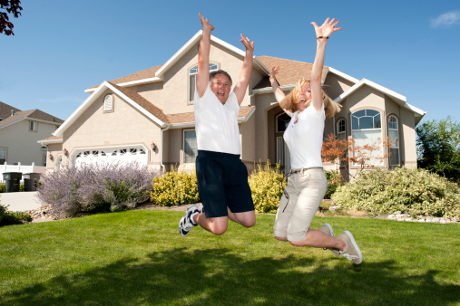 Portrait Of Happy Married Mature Couple Jumping Outside Home