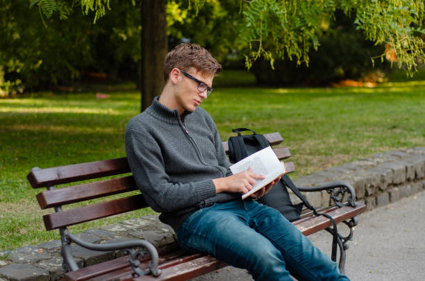 istock Sad depressed teenager sitting on park bench and reading a book 1651679073