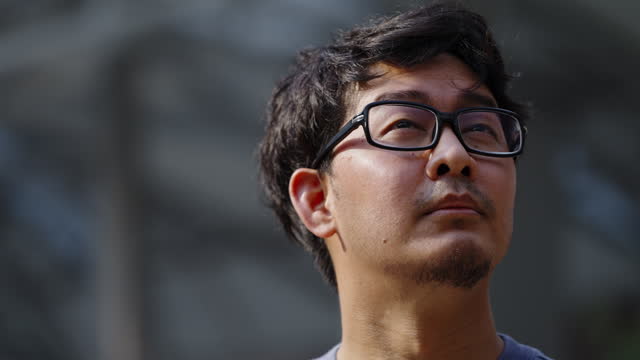 Side view headshot of Asian man looking up to the sky in the city with building background with some hope