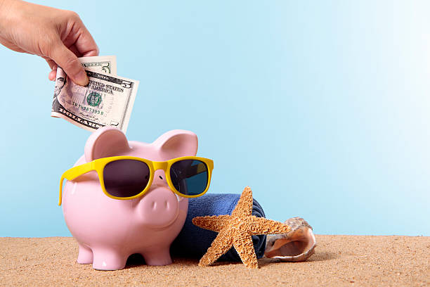 Piggy Bank on beach vacation Saving for beach vacation or retirement, with pink piggy bank and sunglasses.  Studio shot with plain blue background.  Sharp focus on the five dollar bill.  Space for copy.  Warm color and directional lighting are intentional.  Alternative file shown below: five dollar bill stock pictures, royalty-free photos & images