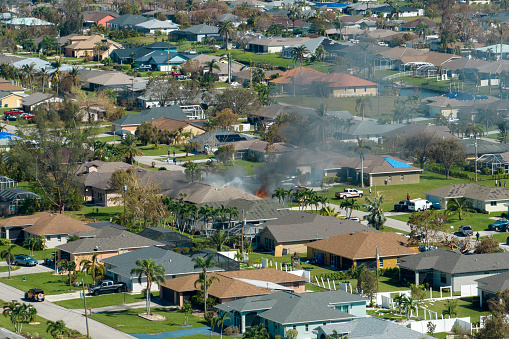 View from above of burning private house on fire and firefighters extinguishing flames after short circuit caused to ignite roof damaged by hurricane Ian wind. Home disaster in Florida suburban area.