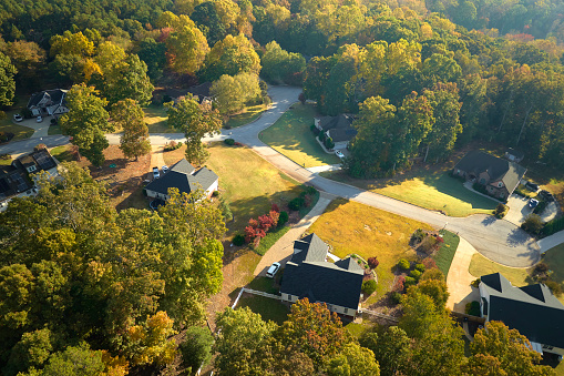 View from above of expensive residential houses between yellow fall trees in suburban area in South Carolina. American dream homes as example of real estate development in US suburbs.